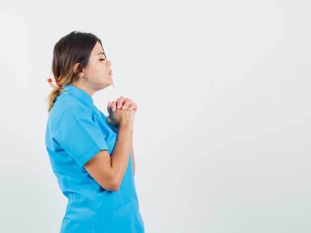 Femme médecin joignant les mains dans un geste de prière en uniforme bleu et l'air calme