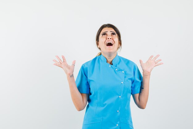 Femme médecin levant les mains en uniforme bleu et l'air excité