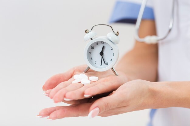 Femme médecin main tenant des pilules et une horloge