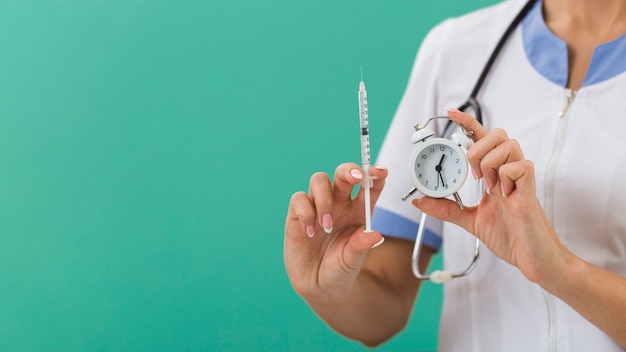 Femme médecin mains tenant une seringue et une horloge
