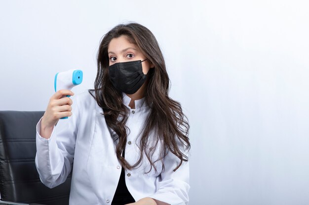 Femme médecin en masque médical tenant un thermomètre et regardant à l'avant.