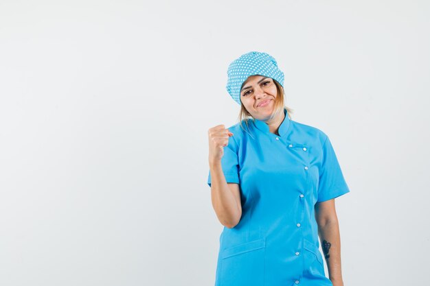 Femme médecin montrant le geste du gagnant en uniforme bleu et l'air heureux