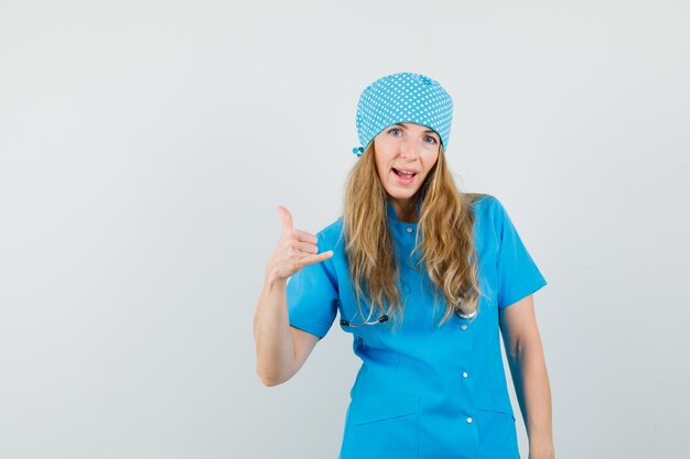 Femme médecin montrant le geste du téléphone en uniforme bleu et à la confiance