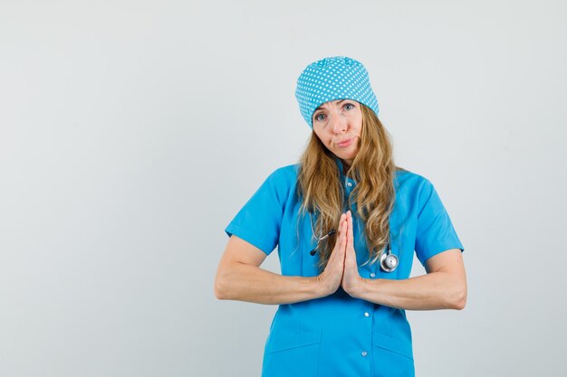 Femme médecin montrant le geste de namaste en uniforme bleu et à la recherche d'impuissance.