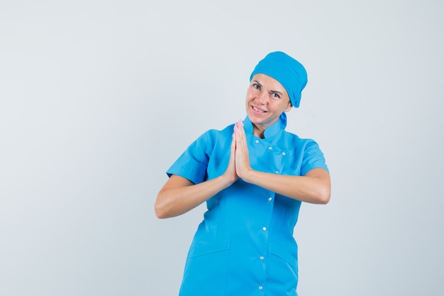 Femme médecin montrant le geste de namaste en uniforme bleu et à la recherche de rêve. vue de face.