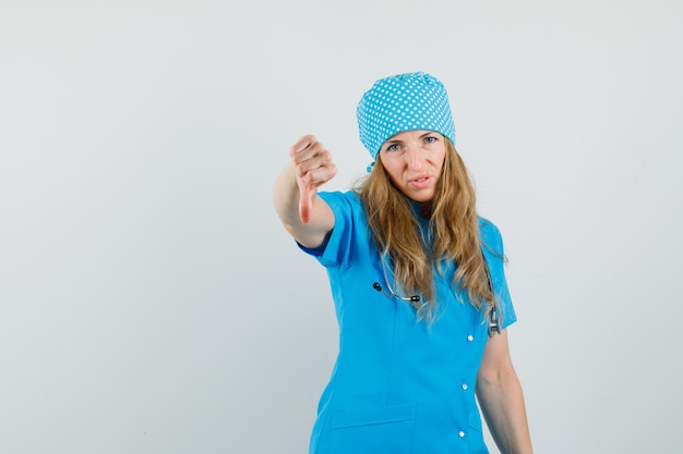 Femme médecin montrant le pouce vers le bas en uniforme bleu et l'air mécontent.