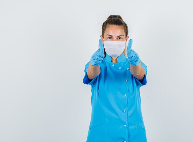 Femme médecin montrant les pouces vers le haut en uniforme bleu