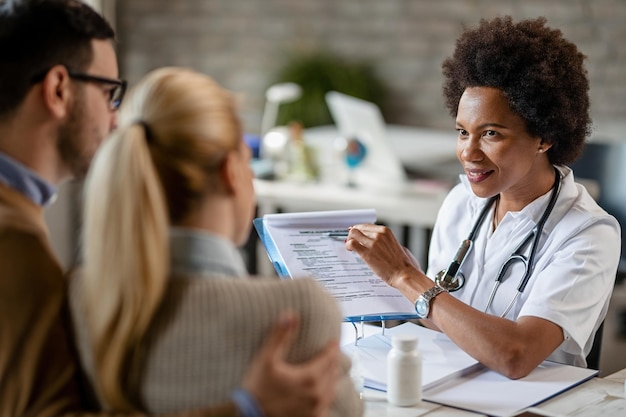 Photo gratuite femme médecin noire souriante parlant à un couple tout en analysant leurs rapports médicaux lors de consultations à la clinique