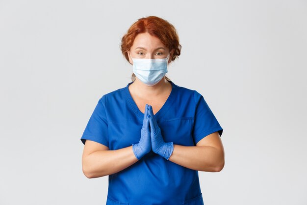 Femme médecin pleine d'espoir, médecin rousse ou infirmière demandant de l'aide, se tenant la main pour plaider, porter un masque et des gants, rester à la maison s'il vous plaît