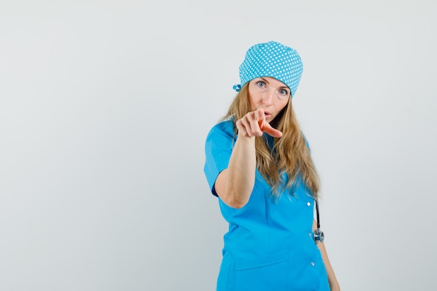 Femme médecin pointant la caméra en uniforme bleu et à la perplexité.