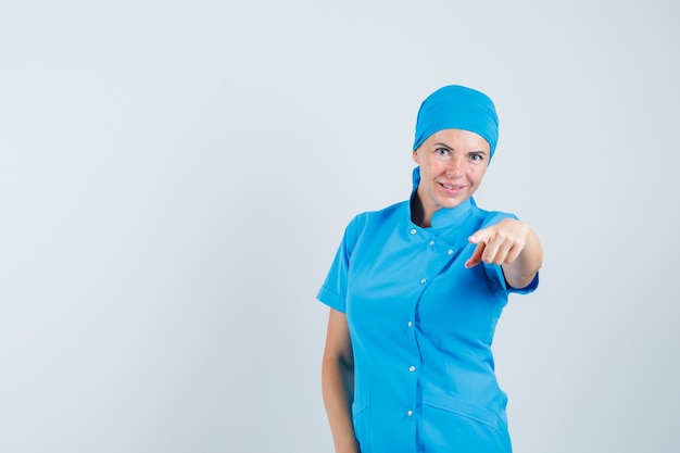 Femme médecin pointant la caméra en uniforme bleu et à la recherche de confiance. vue de face.