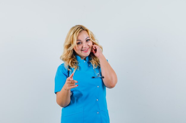 Femme médecin pointant la caméra en uniforme bleu et à la recherche d'optimiste.