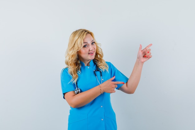 Femme médecin pointant de côté en uniforme bleu et l'air heureux.