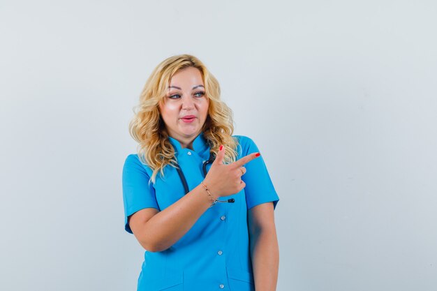 Femme médecin pointant de côté en uniforme bleu et à la recherche concentrée