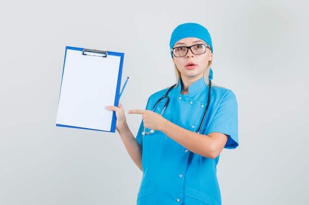 Femme médecin pointant le doigt au presse-papiers en uniforme bleu