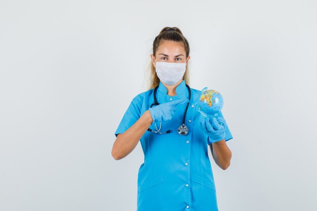 Femme médecin pointant le doigt sur le globe terrestre en uniforme bleu