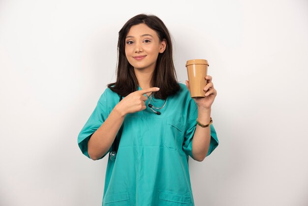 Femme médecin pointant la tasse de café sur fond blanc. Photo de haute qualité