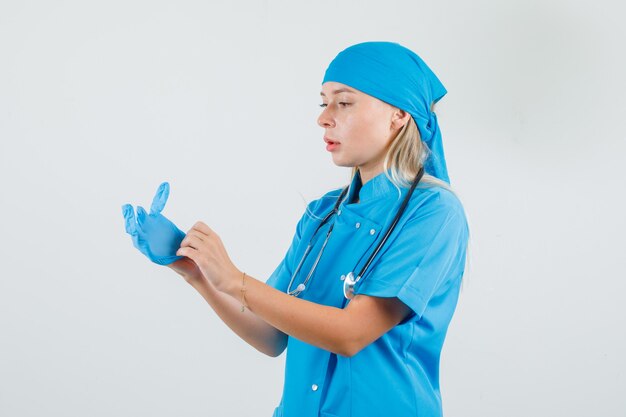 Femme médecin portant des gants médicaux en uniforme bleu et regardant attentivement.