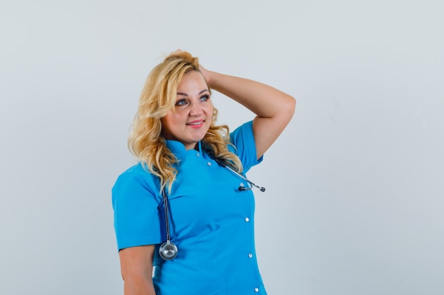 Femme médecin posant avec la main sur la tête en uniforme bleu et à la recherche de brillant