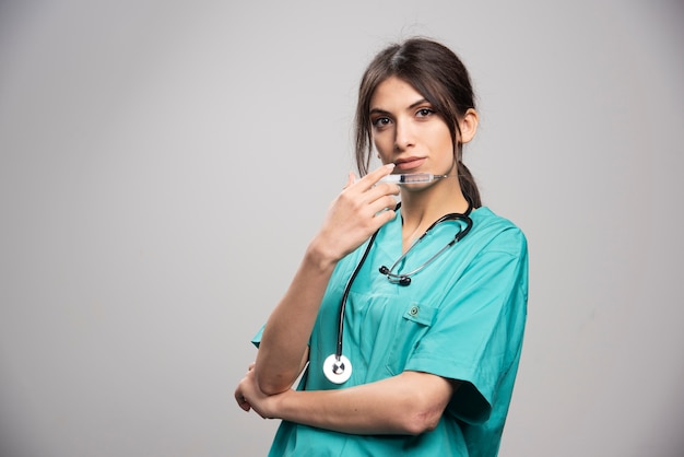 Femme médecin posant avec une seringue sur fond gris