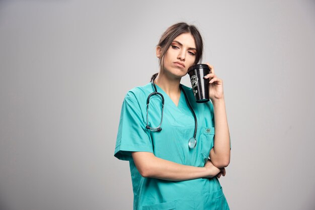 Femme médecin posant avec une tasse de café sur fond gris