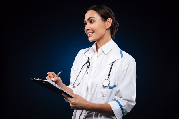 Femme médecin positive écrit dans le presse-papiers et regarde de côté