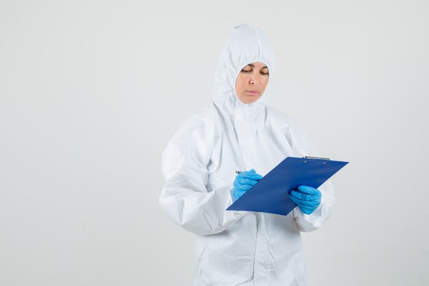 Femme médecin prenant des notes sur le presse-papiers en combinaison de protection