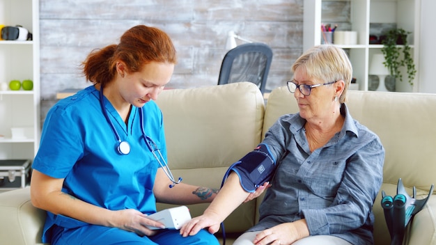 Femme médecin prenant la pression artérielle d'une femme âgée en maison de retraite assise sur un canapé