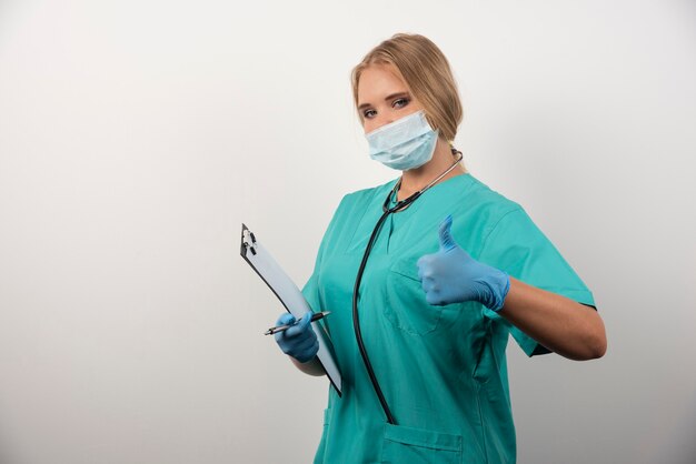 Femme médecin avec presse-papiers montrant le pouce vers le haut.