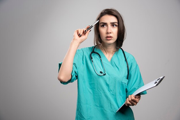 Femme médecin avec presse-papiers pensant à l'opération. Photo de haute qualité