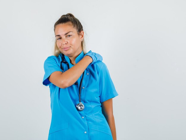 Femme médecin se frottant l'épaule pour se détendre en uniforme bleu