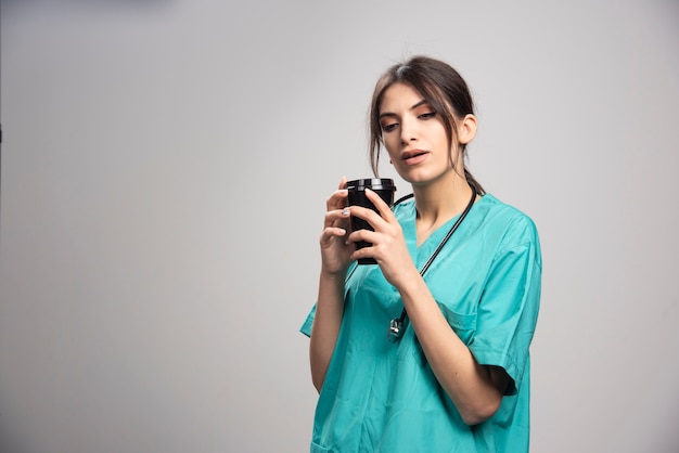 Femme médecin sent l'arôme du café sur fond gris