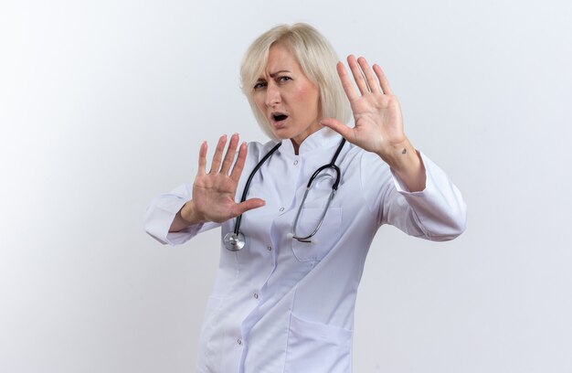 Femme médecin slave adulte agacée en robe médicale avec stéthoscope debout avec les mains levées isolées sur fond blanc avec espace de copie