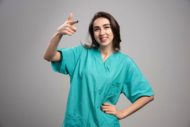 Femme médecin souriante pointant la caméra sur fond gris. Photo de haute qualité