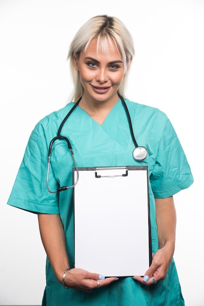 Photo gratuite femme médecin souriante tenant un presse-papiers sur une surface blanche