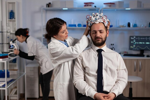 Femme médecin spécialiste mettant un casque eeg sur un patient homme surveillant l'évolution du cerveau analysant l'activité du système nerveux en laboratoire clinique. Docteur en neurosciences faisant la tomographie médicale