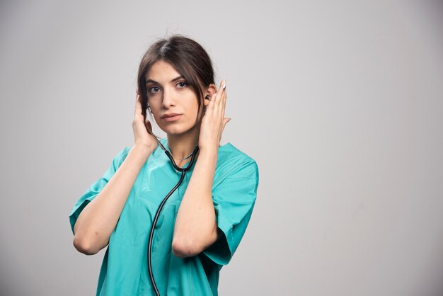 Femme médecin avec stéthoscope debout sur fond gris