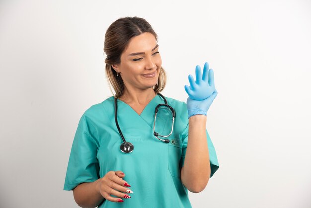 Femme médecin avec stéthoscope portant des gants en latex sur fond blanc.