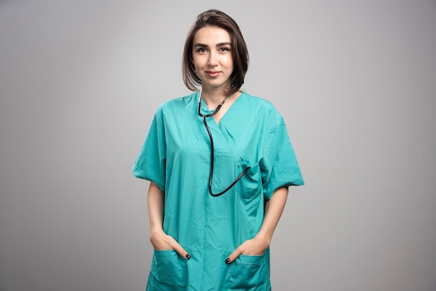 Femme médecin avec stéthoscope posant sur fond gris. Photo de haute qualité