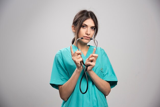 Femme médecin avec stéthoscope posant sur fond gris
