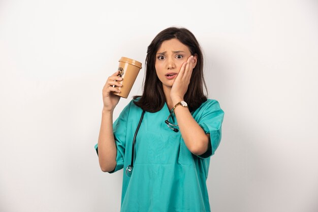 Femme médecin avec une tasse de café tenant sa joue sur fond blanc.