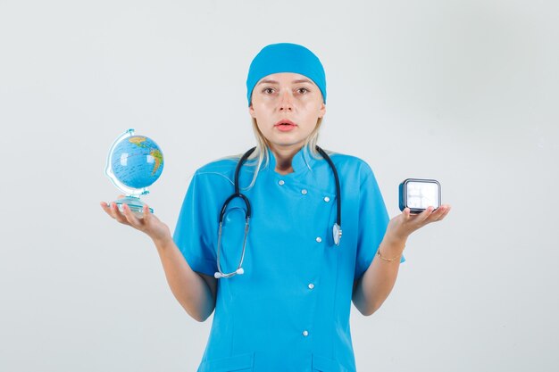 Femme médecin tenant le globe terrestre et horloge en uniforme bleu et à la grave