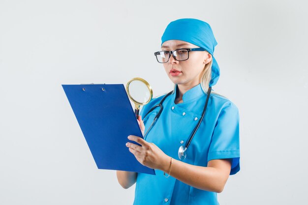 Femme médecin tenant la loupe sur le presse-papiers en uniforme bleu