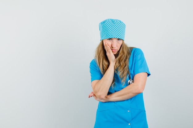 Femme médecin tenant la main sur la joue en uniforme bleu et à la pensif