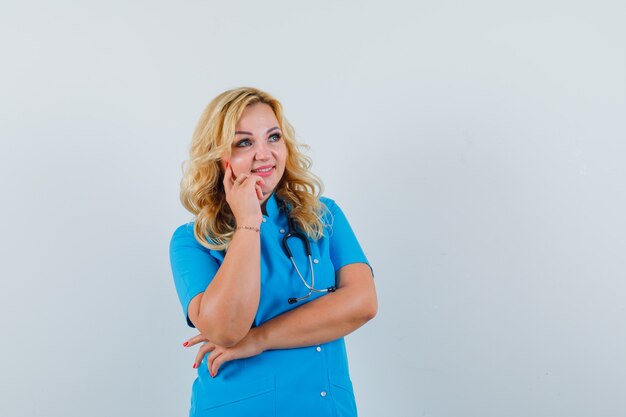 Femme médecin tenant la main sur son menton tout en regardant ailleurs en uniforme bleu et à l'espace intéressé pour le texte