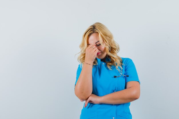 Femme médecin tenant la main sur son nez tout en fermant les yeux en uniforme bleu et à la fatigue. espace pour le texte