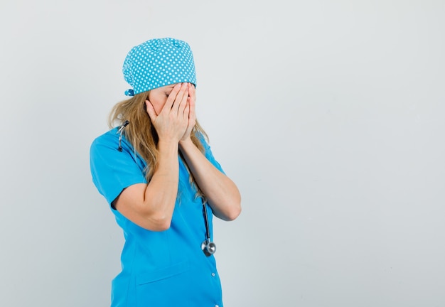 Femme médecin tenant la main sur le visage en uniforme bleu et à la recherche de calme