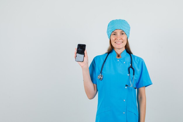 Femme médecin tenant le smartphone en uniforme bleu et à la joyeuse