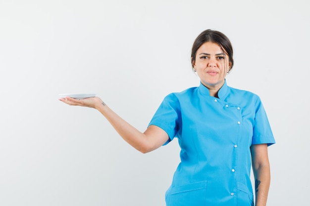 Femme médecin tenant une soucoupe blanche en uniforme bleu et ayant l'air confiant