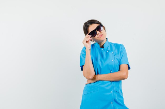 Femme médecin touchant ses lunettes en uniforme bleu et semblant jolie